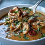 Creamy Thai coconut curry soup bowl with tender chicken, mushrooms, and carrots in a fragrant red curry broth, garnished with fresh cilantro and lime.  