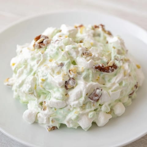 A bowl of vibrant Watergate Salad with green pistachio pudding, marshmallows, and pecans.