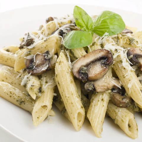 Fork twirling a bite of mushroom pesto pasta with golden sautéed cremini mushrooms.