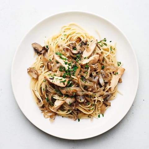 Shiny, golden chicken strips rest atop slender spaghettini tossed in a velvety mushroom cream sauce, garnished with parsley.