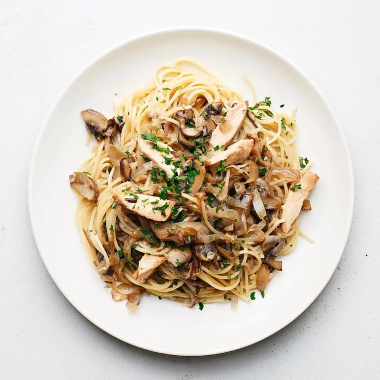 Shiny, golden chicken strips rest atop slender spaghettini tossed in a velvety mushroom cream sauce, garnished with parsley.