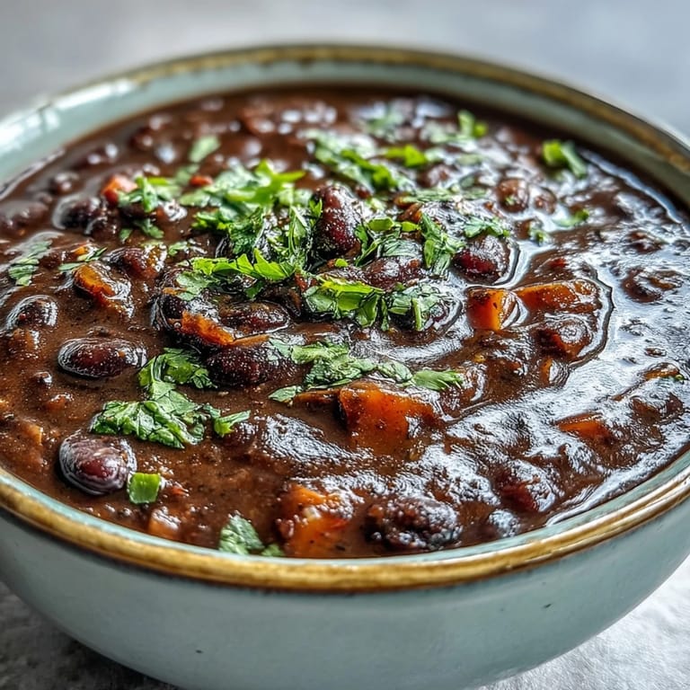 Black bean soup in a rustic ceramic bowl, steam rising from the thick texture with a sprinkle of diced red onion garnish.