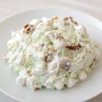 A bowl of vibrant Watergate Salad with green pistachio pudding, marshmallows, and pecans.