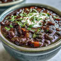 Creamy black bean soup simmering in a pot, garnished with fresh cilantro, sour cream, and sliced avocado for a comforting Latin American meal.